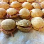 Close-up of dozens of golden-brown sweet potato biscuits, each sliced and filled with thinly shaved country ham, sitting in a foil catering pan lined with parchment paper.